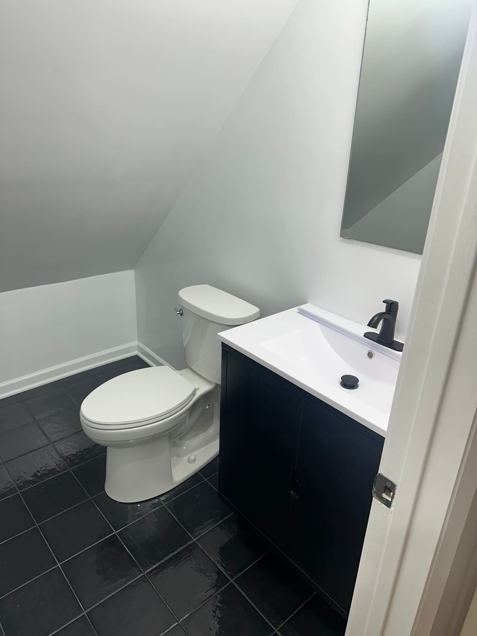 Navy vanity with a white basin and mirror set beneath the slope of the attic ceiling, next to the toilet.