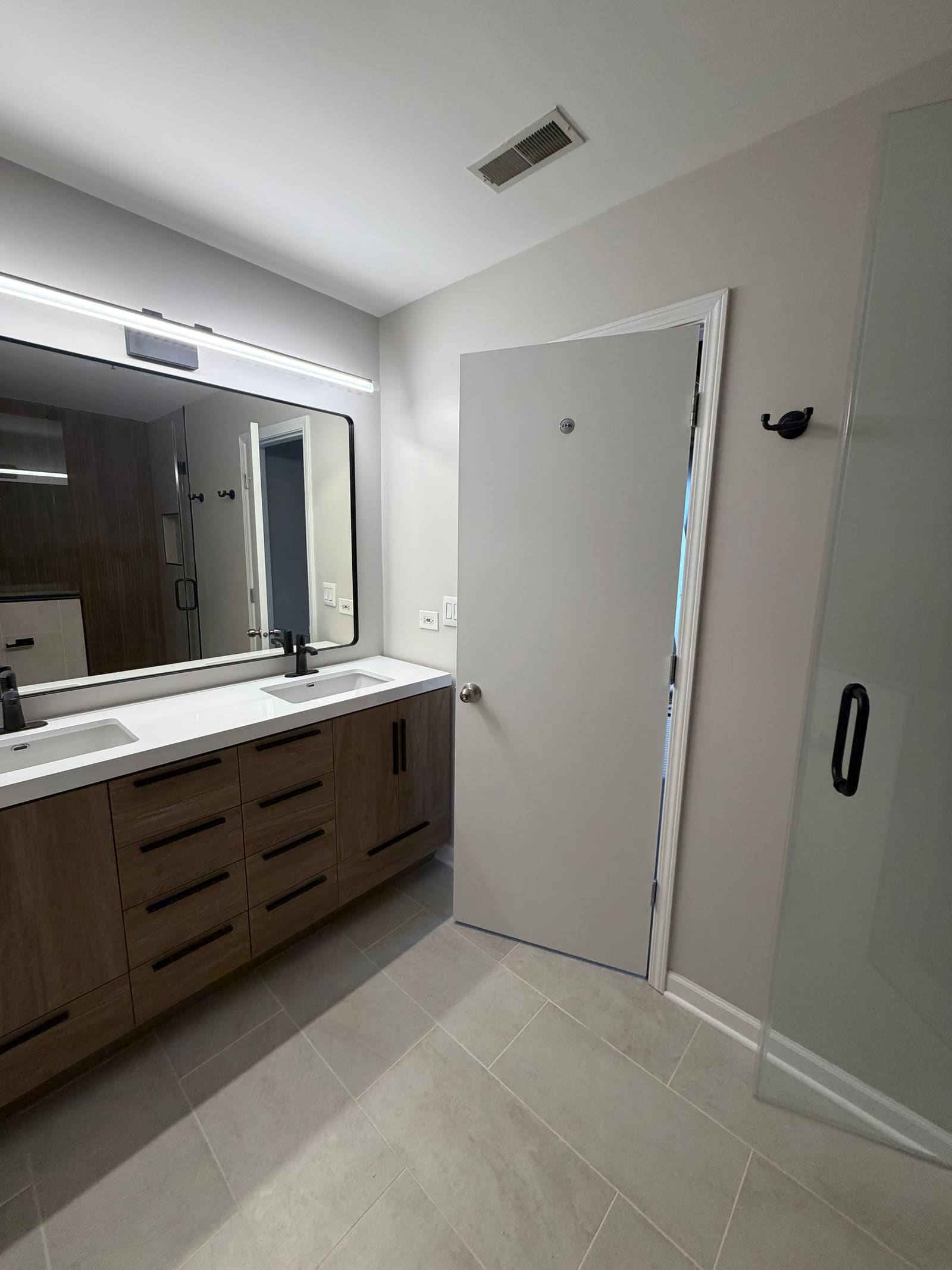 Two-sink vanity in dark wood with a white quartz top, black hardware, and a wide lit mirror.
